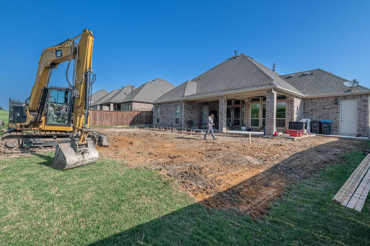 A bare graded back yard with an excavator parked on the cut