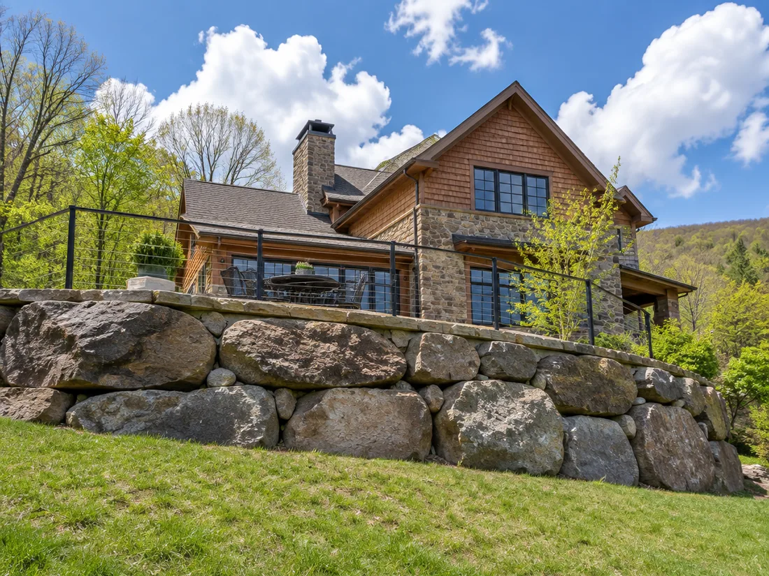 A stone terrace carried on a boulder-faced retaining wall above a grass bank on a bright spring day